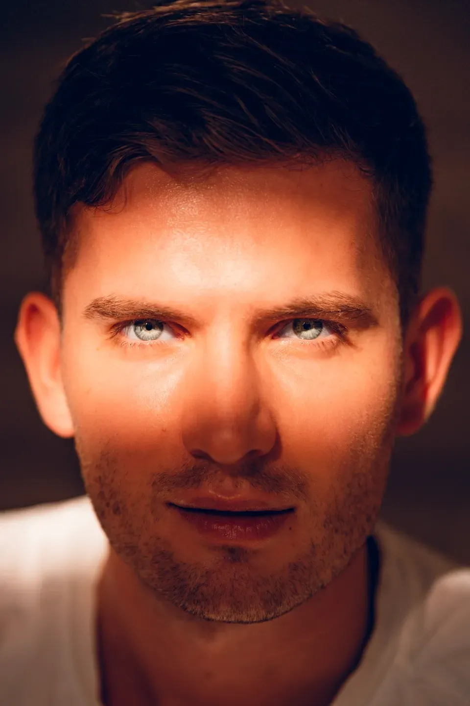 Nahaufnahme eines Männergesichts mit hellen Augen, ein warmer Lichtstreifen fällt quer über die Augenpartie