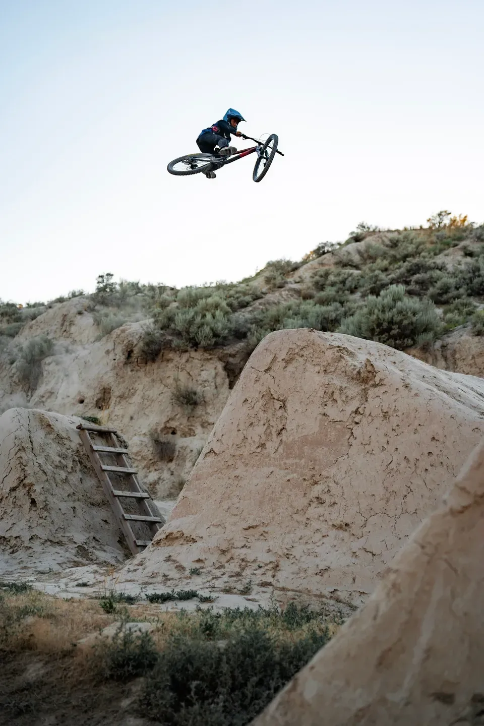 Mountainbiker im Whip hoch über Erdsprüngen mit Holzleiter, Hochformat mit viel Himmel