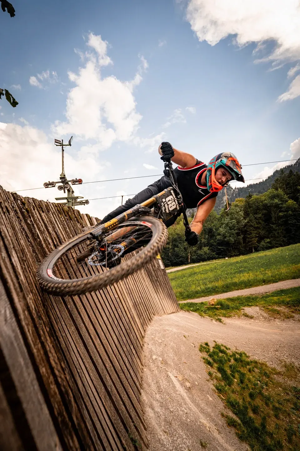 Mountainbiker fährt in Schräglage an einer hölzernen Steilwand, Froschperspektive mit blauem Himmel