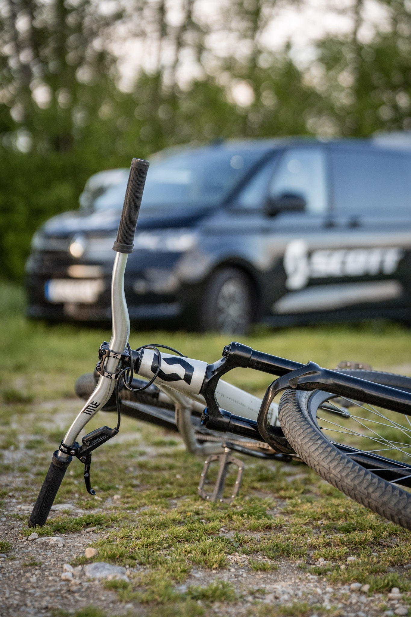Lenker eines liegenden Dirtbikes im Vordergrund, dahinter unscharf ein dunkler Transporter mit Scott-Schriftzug