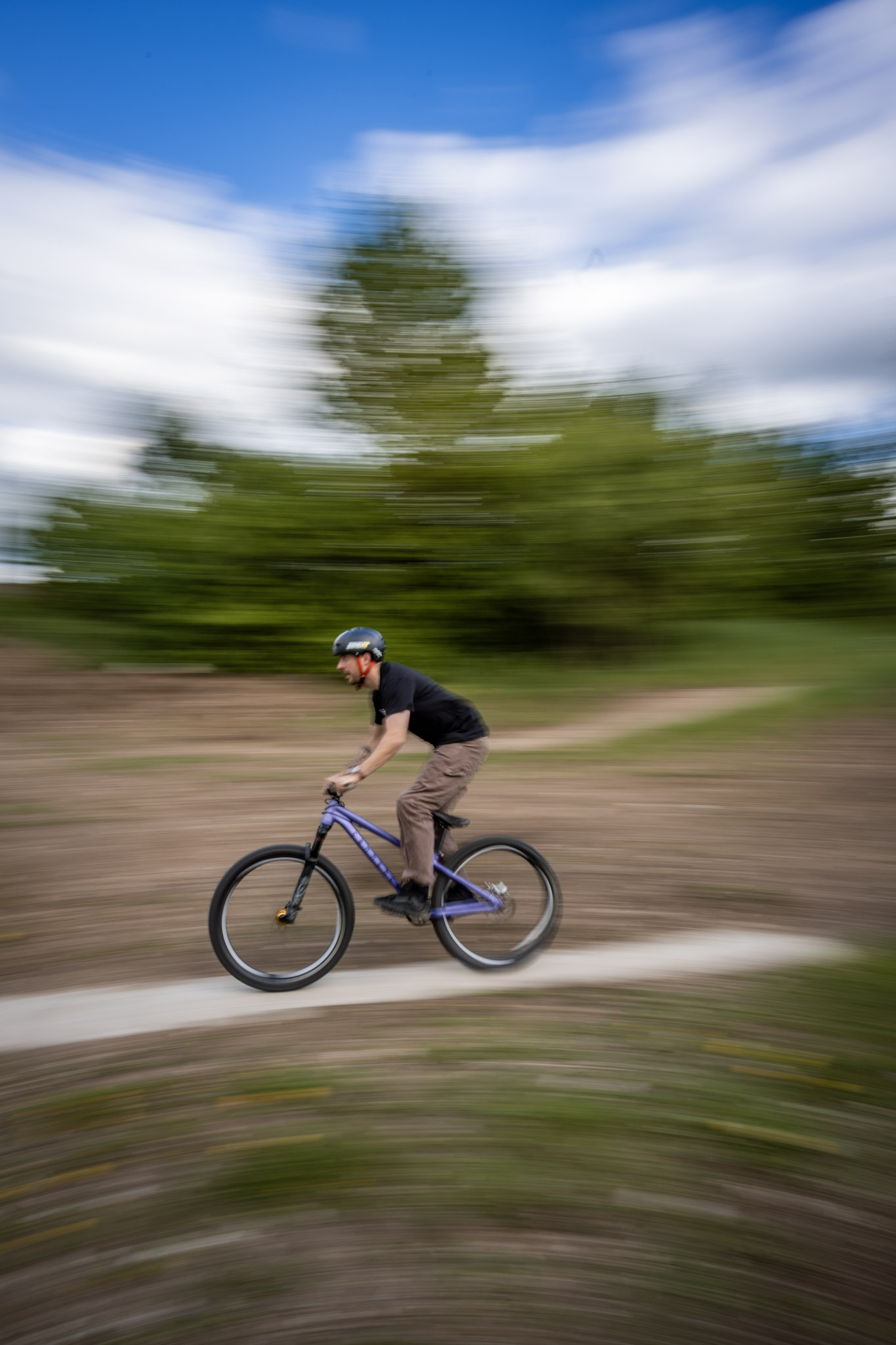 Dirtbiker fährt mit lila Bike über einen Feldweg, Hintergrund durch Mitzieher verwischt