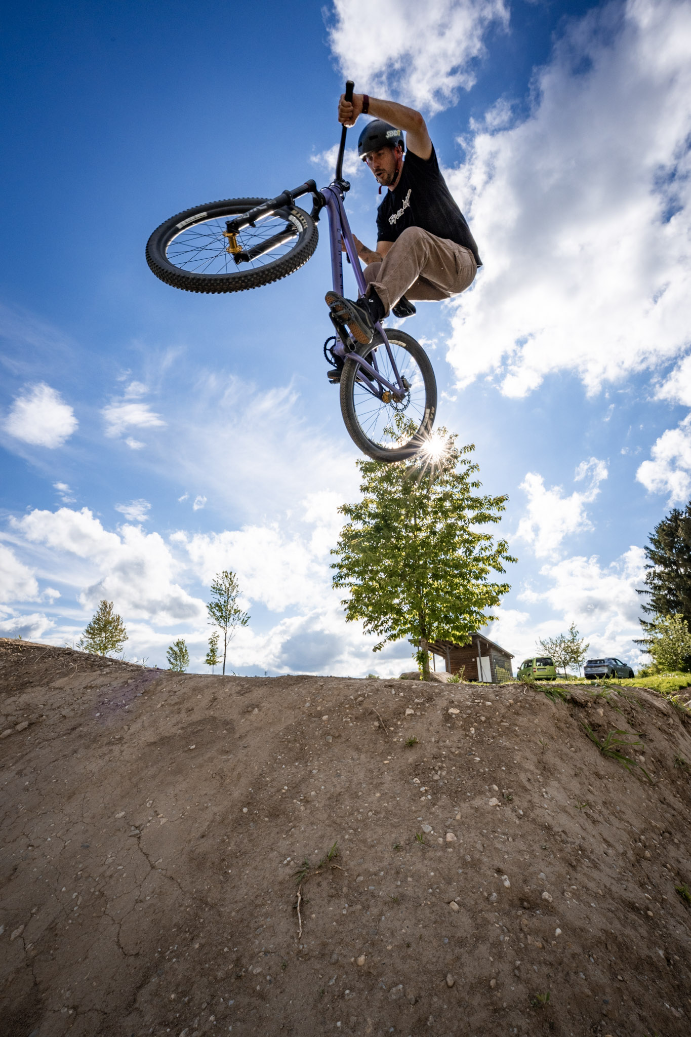 Dirtbiker reißt das Bike im Sprung zur Seite, Froschperspektive mit Sonnenstern und weißen Wolken