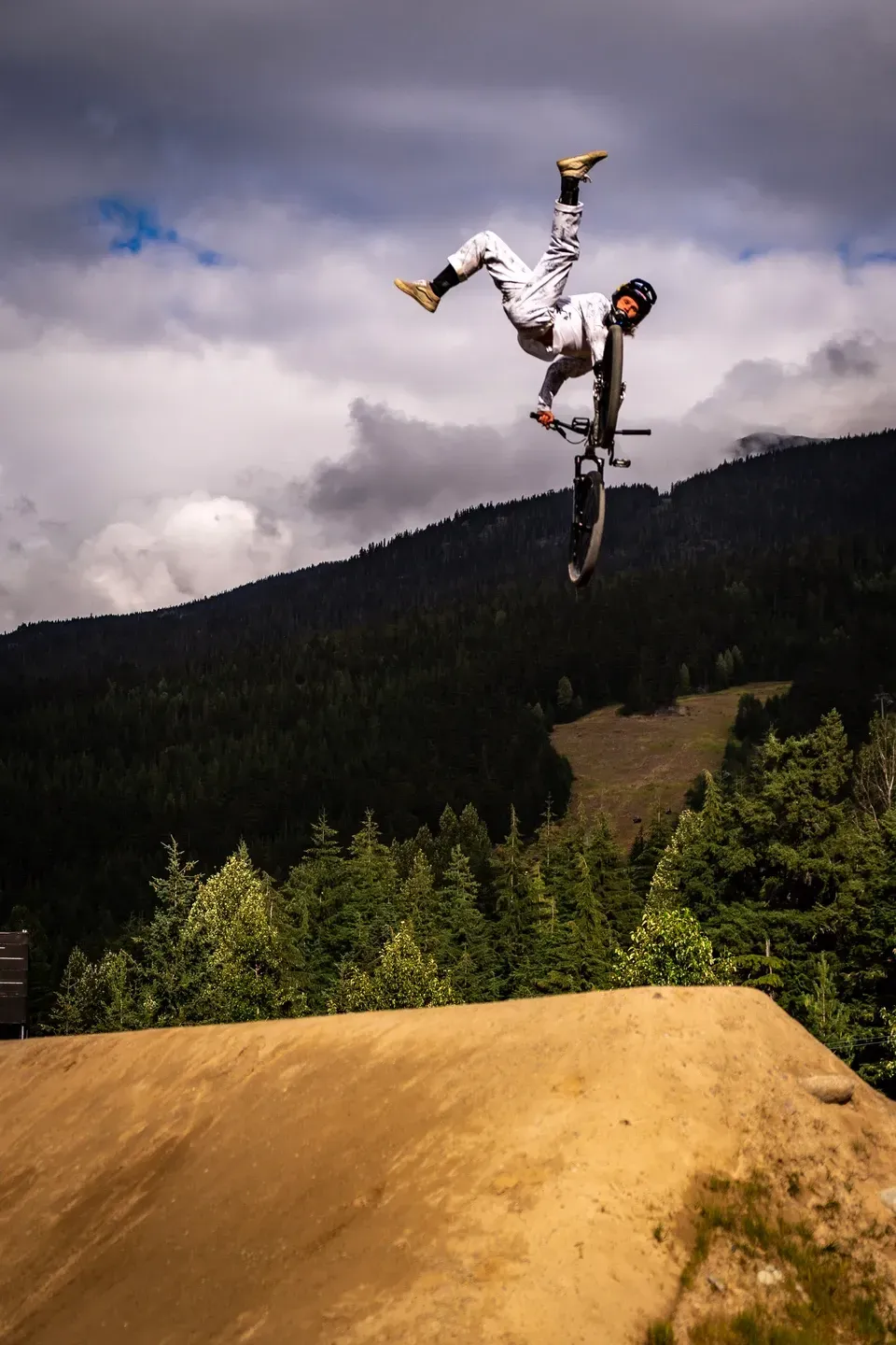 Dirtbiker streckt im Sprung die Beine in die Luft und hält nur den Lenker, dahinter Berghang und Wolken