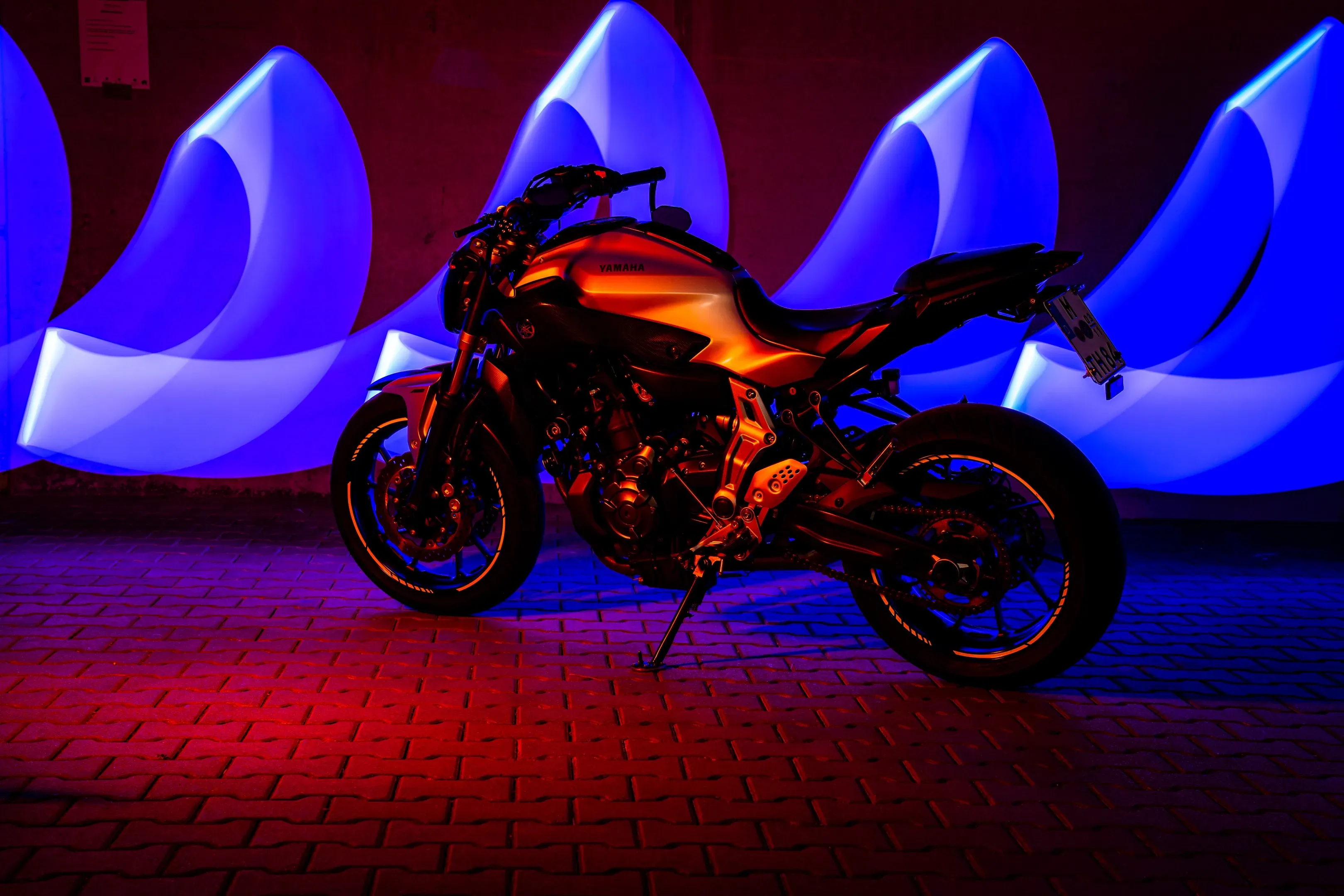 Yamaha Naked Bike auf Pflaster bei Nacht, hinter dem Motorrad leuchten blaue Lightpainting-Bögen