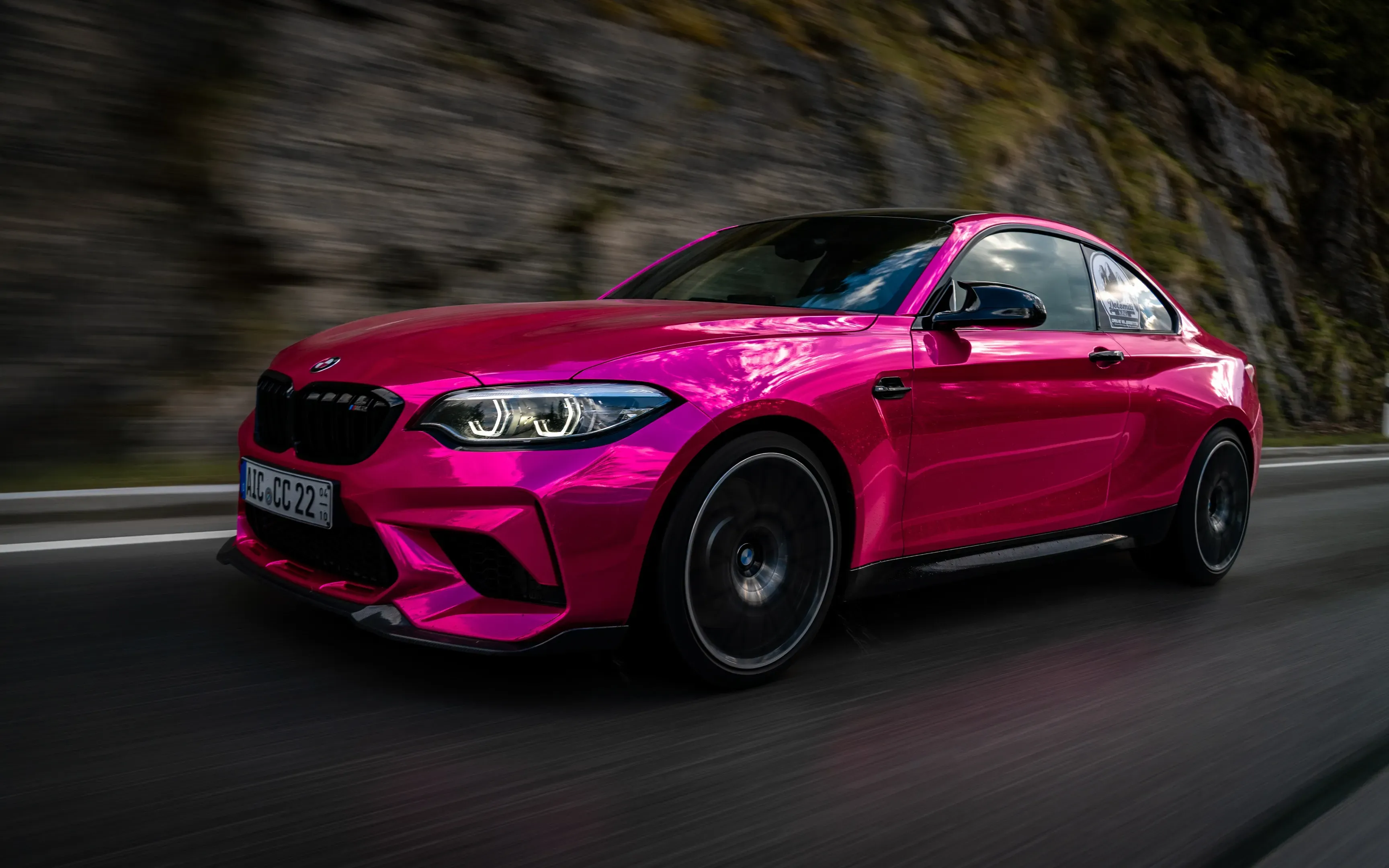 Pinker BMW M2 in Fahrt auf einer Straße entlang einer Felswand, Hintergrund durch Bewegung verwischt