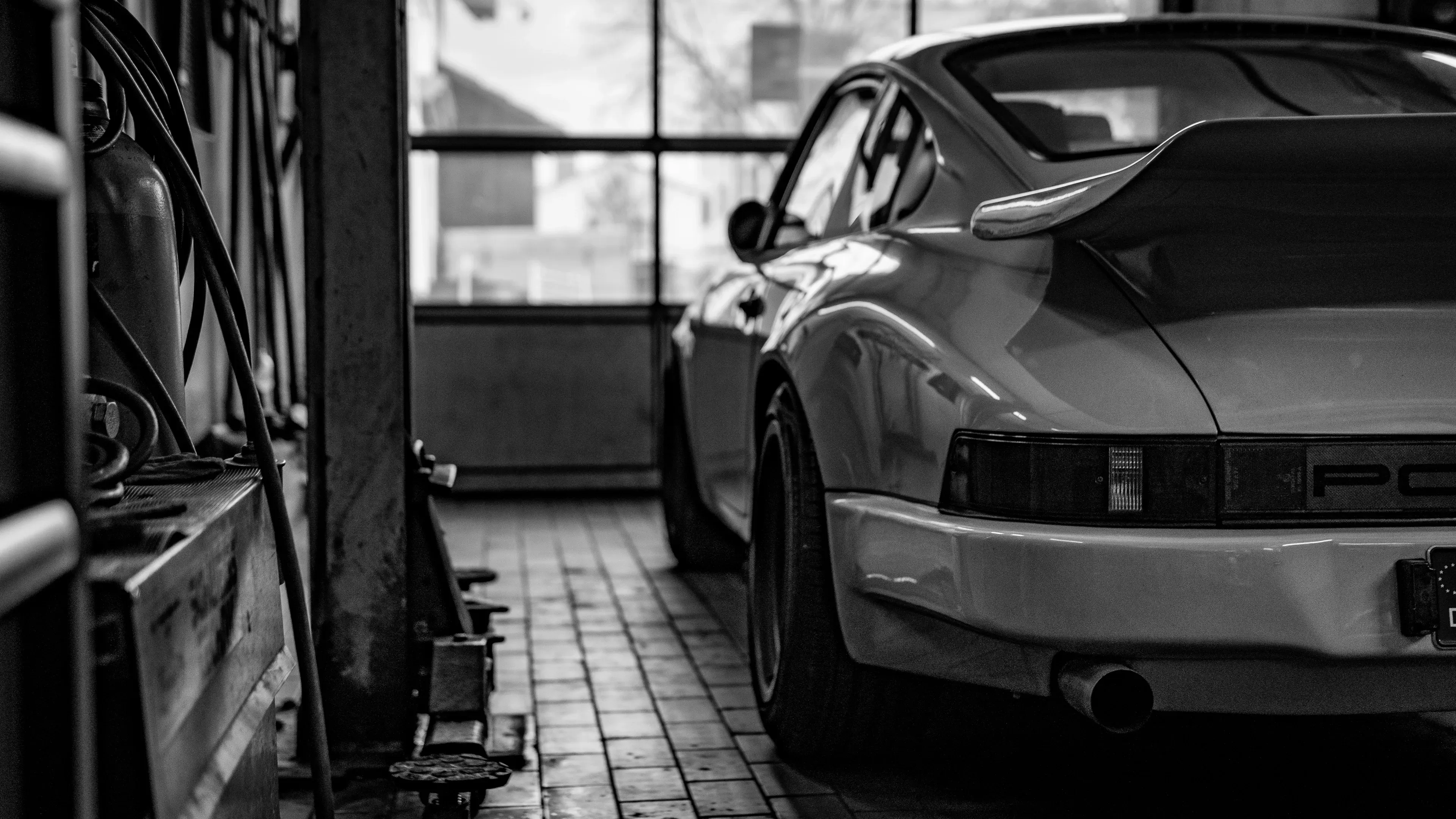 Schwarzweißaufnahme vom Heck eines klassischen Porsche 911 mit Heckspoiler in einer alten Werkstatt