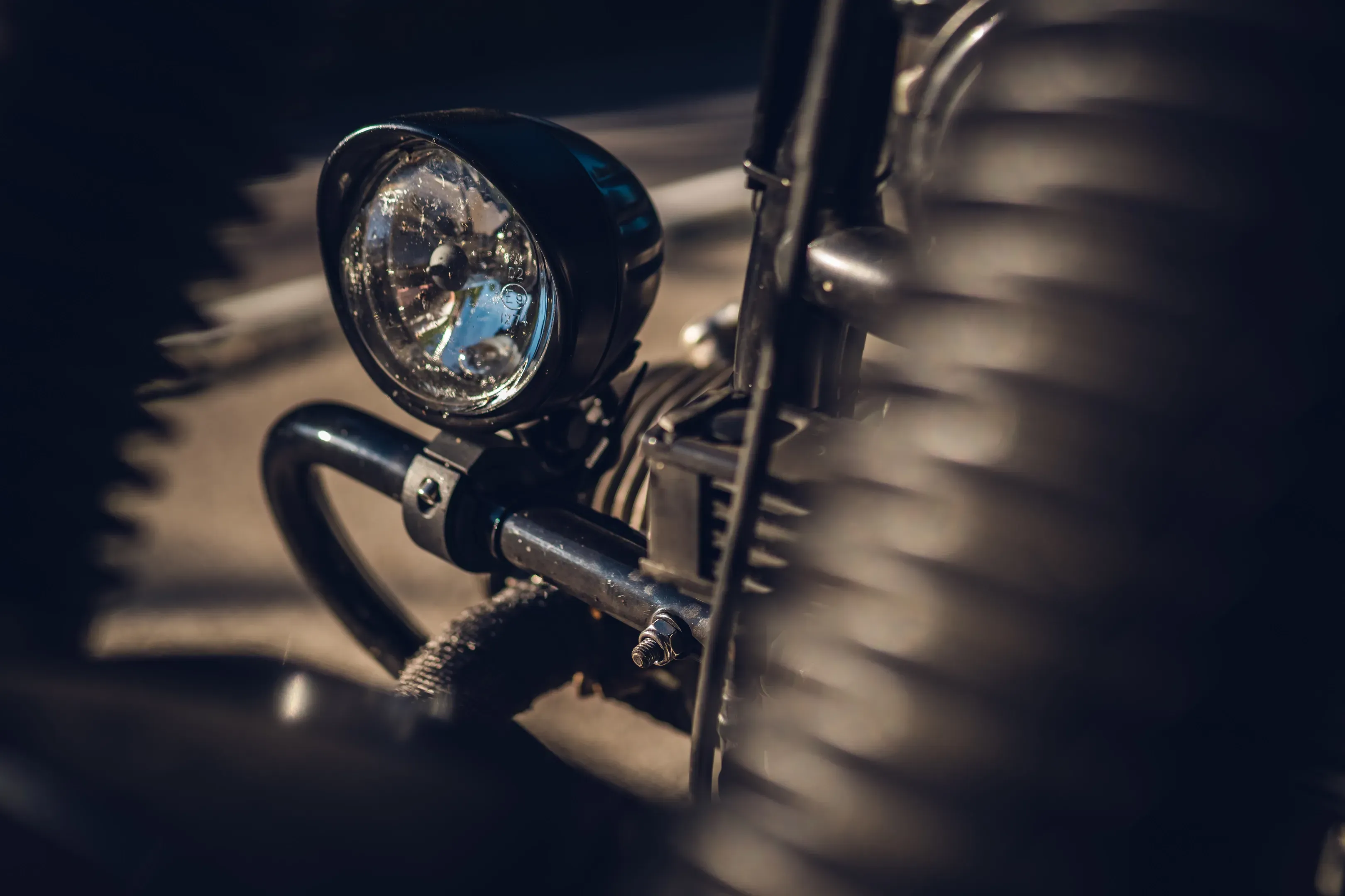 Runder Scheinwerfer eines Custom-Motorrads im Streiflicht, seitlich unscharf der gerippte Reifen