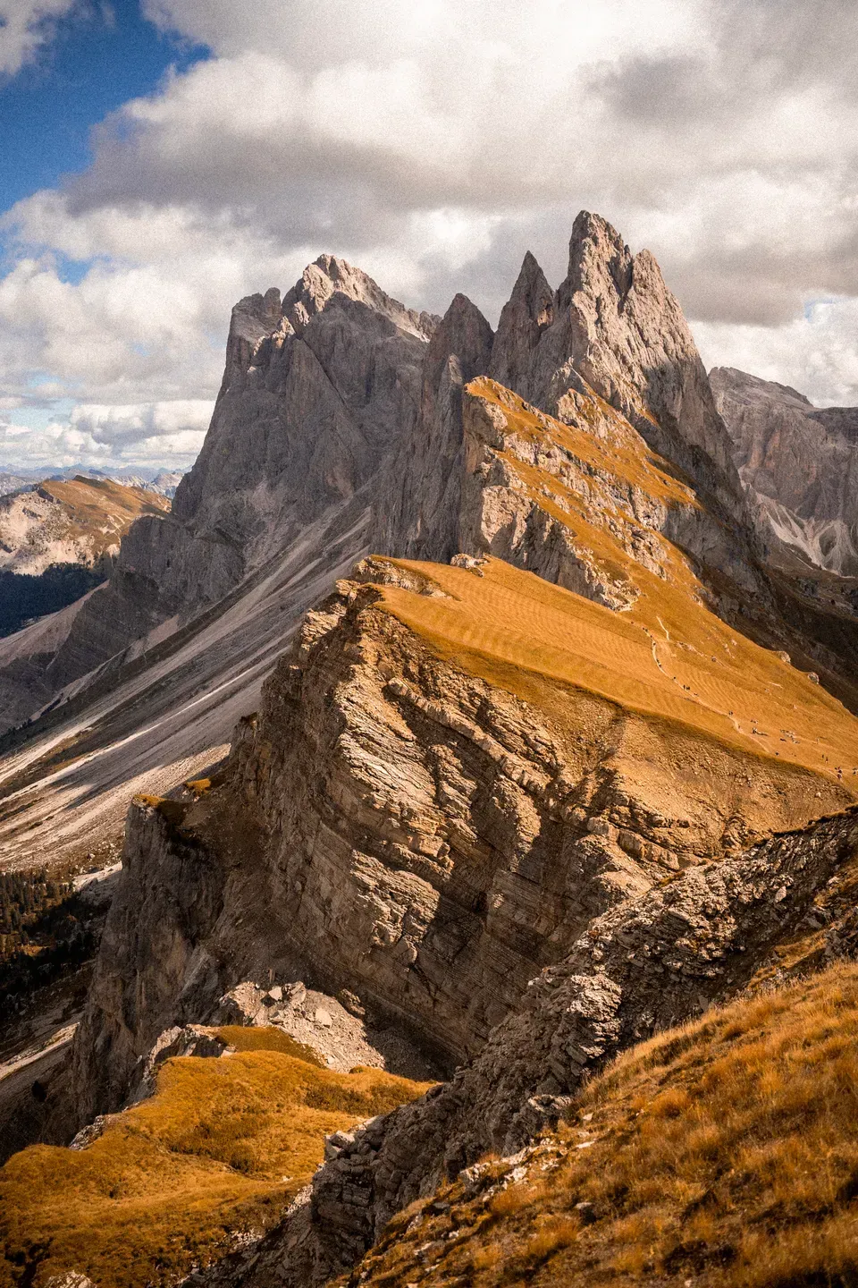 Grasbewachsener Bergrücken der Seceda mit steil abfallenden Felszacken unter Wolken im Herbstlicht