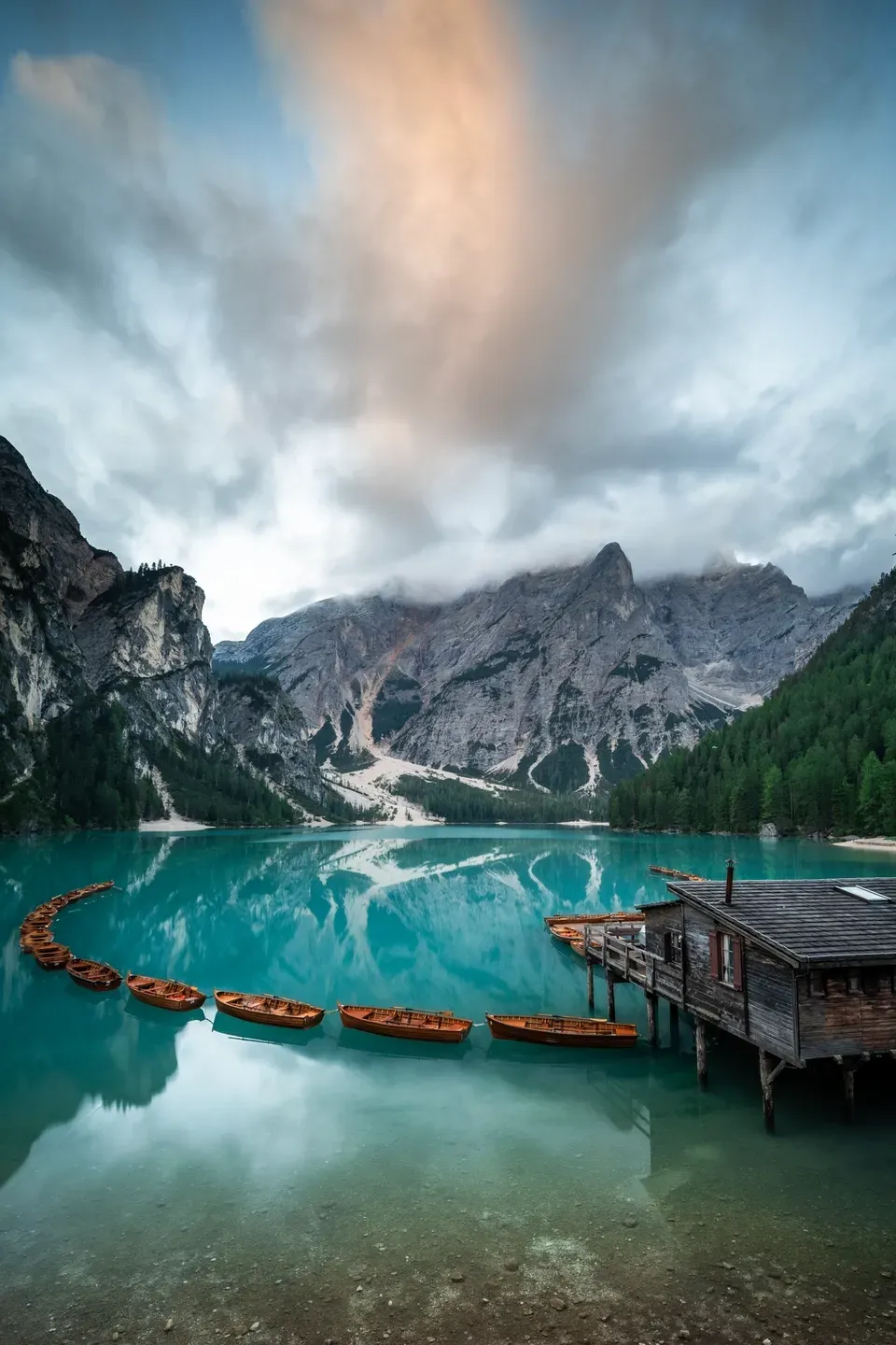 Ruderboote und Bootshaus am Pragser Wildsee im Hochformat, über den Bergen eine rötlich angestrahlte Wolke