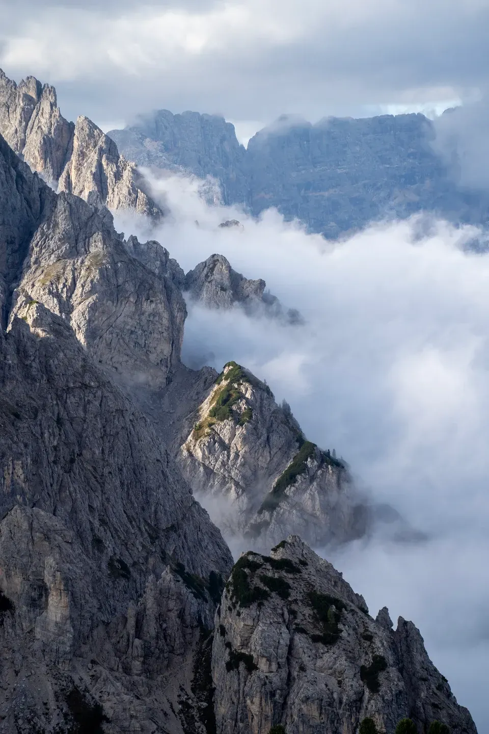 Zerklüftete Felsgrate der Dolomiten ragen aus einem Wolkenmeer, seitliches Licht auf den Felskanten