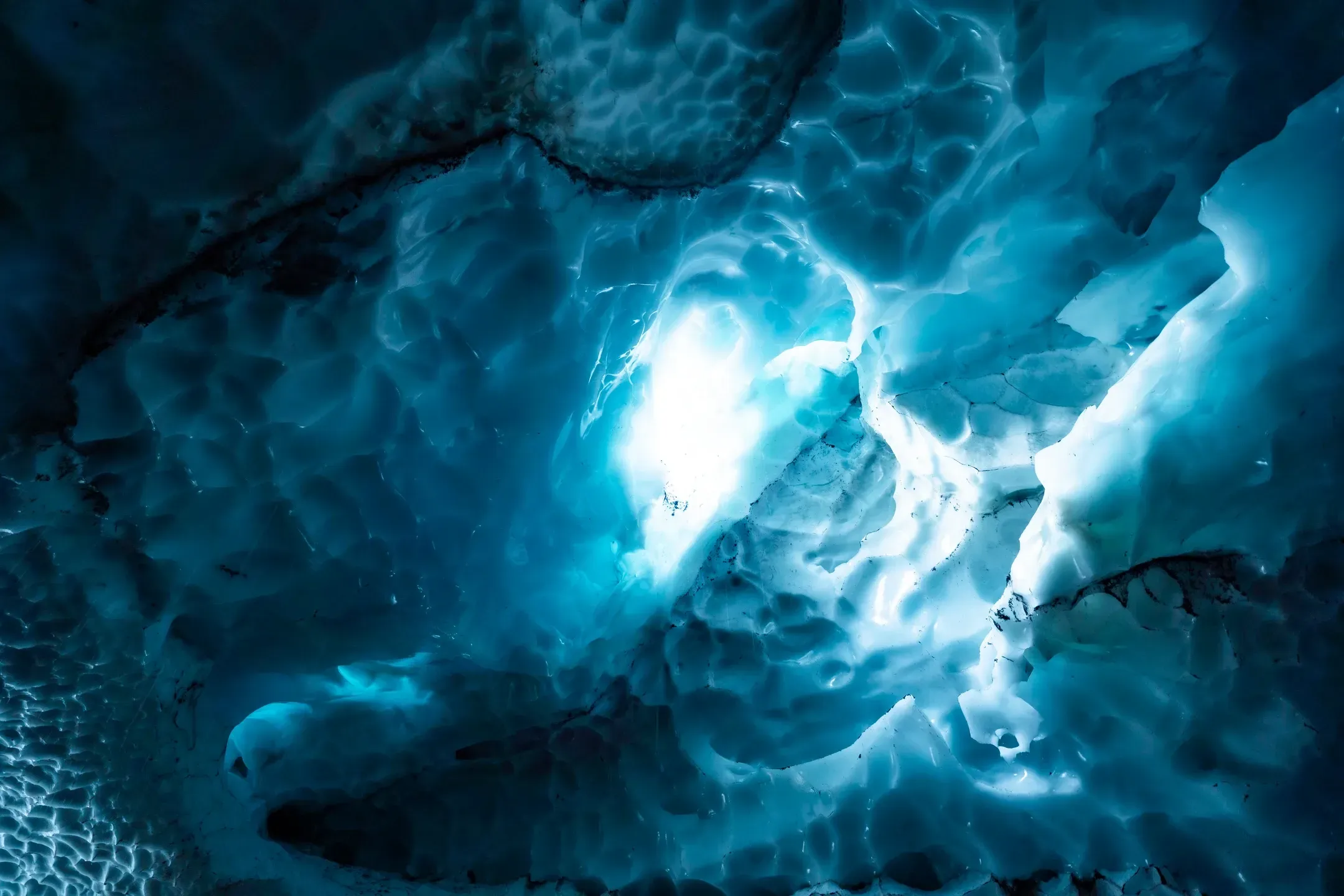Gewölbte Decke einer Eishöhle mit wabenartiger Struktur, das Licht leuchtet türkis durch das Eis