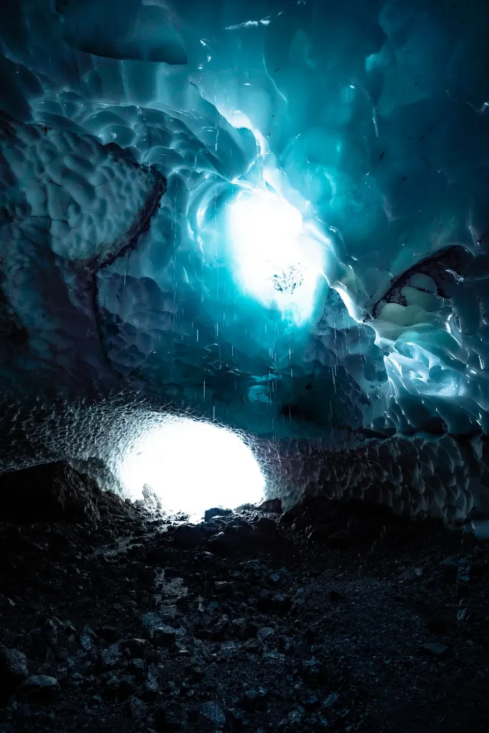 Eishöhle mit hellem Ausgang am Boden, Schmelzwasser tropft von der leuchtend blauen Eisdecke