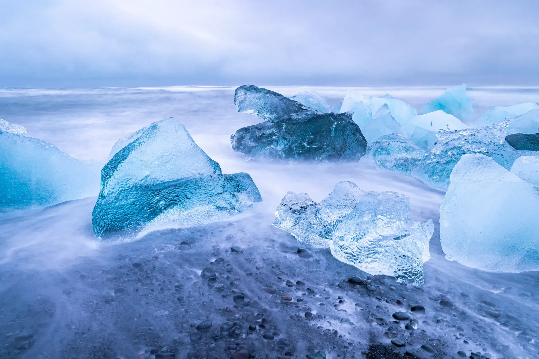 Klare Eisbrocken am schwarzen Strand, von weich verschwommenen Wellen umspült