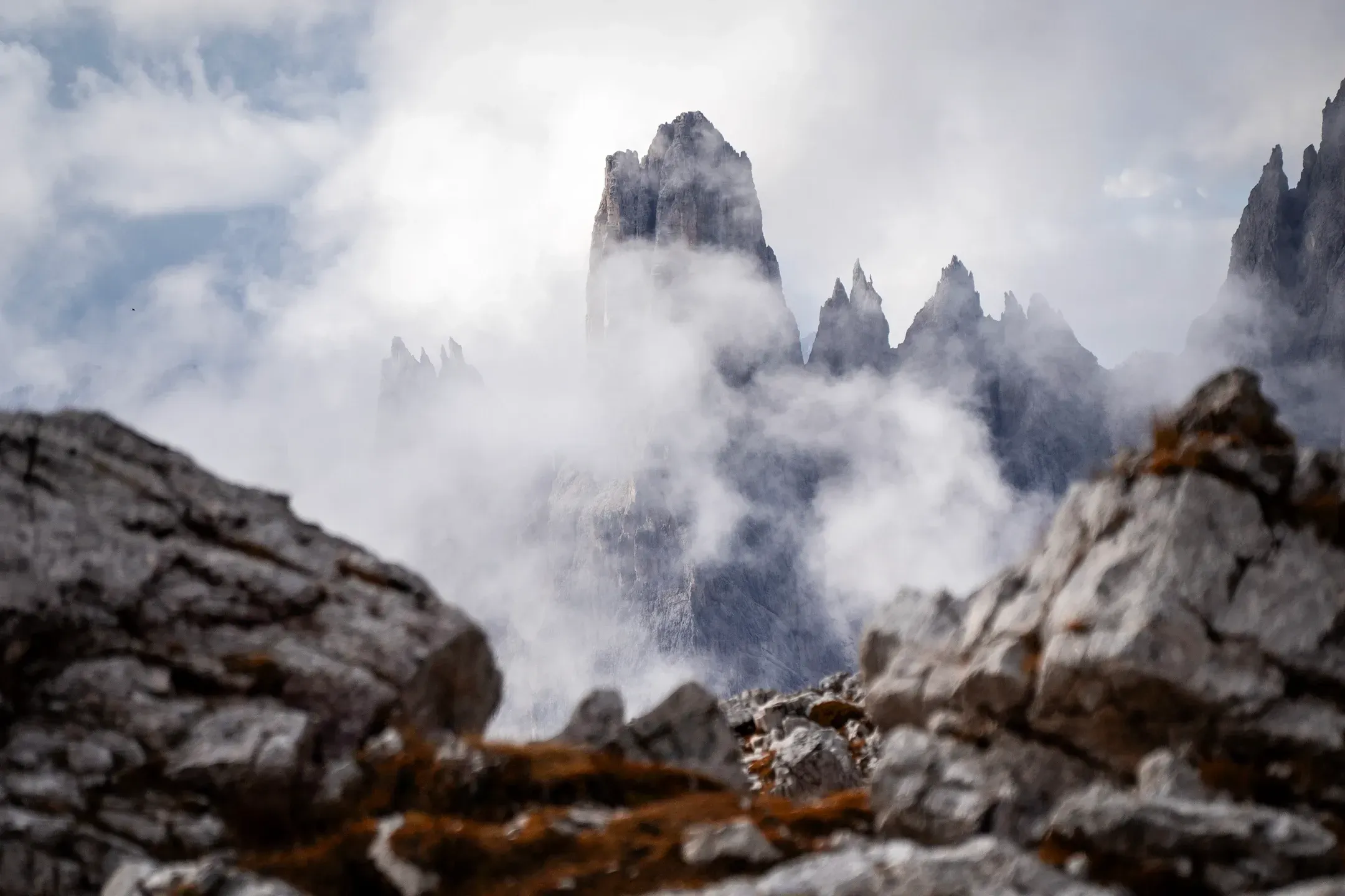 Spitze Dolomitengipfel tauchen aus Nebelschwaden auf, vorne unscharfe Kalksteinblöcke