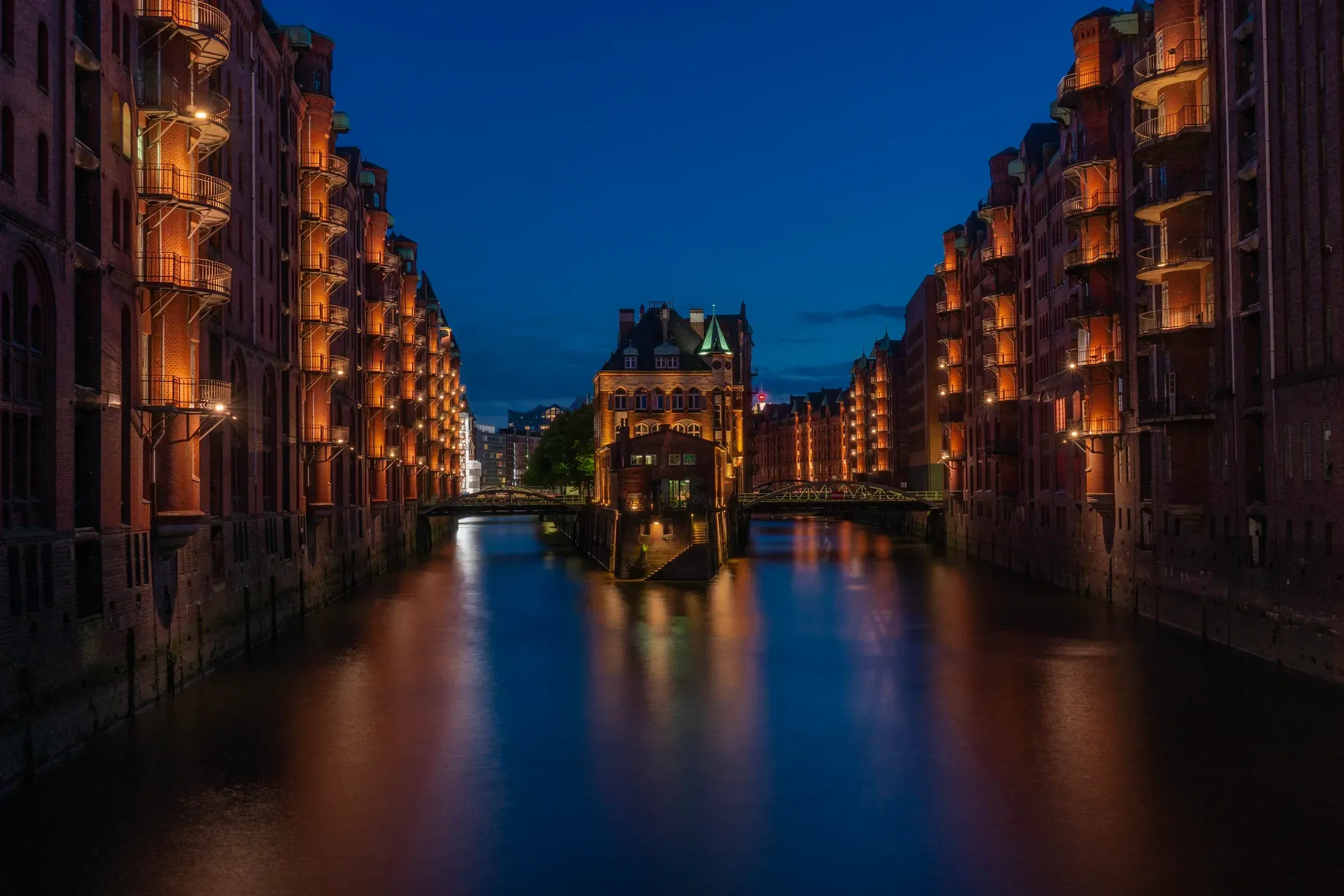 Beleuchtete Backsteinspeicher der Speicherstadt in Hamburg spiegeln sich in der blauen Stunde im Fleet