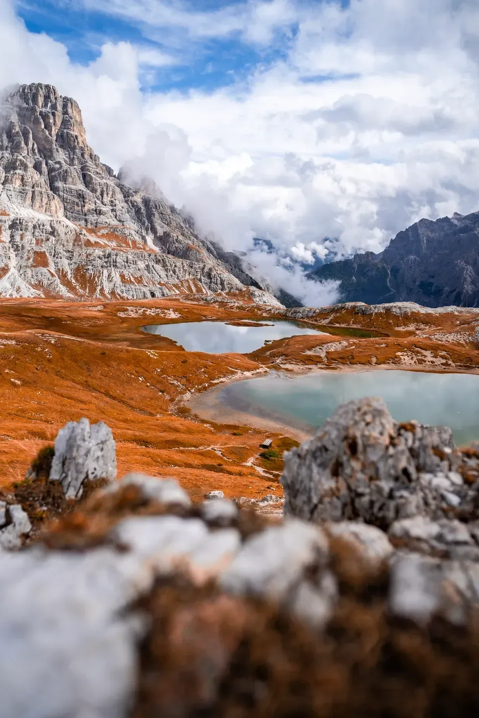 Kleine Bergseen auf einem herbstlich orangen Hochplateau unter schroffen Kalkgipfeln und aufziehenden Wolken
