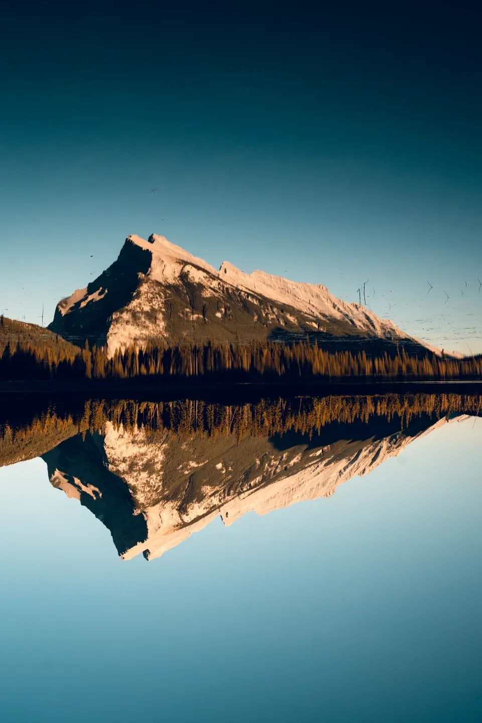 Auf den Kopf gestellte Aufnahme eines Felsgipfels, der sich mit dem Waldsaum in einem spiegelglatten See spiegelt