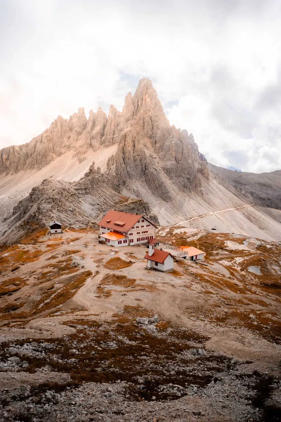 Berghütte mit roten Dächern auf einem herbstlichen Geröllplateau unter einem zackigen Felsgipfel